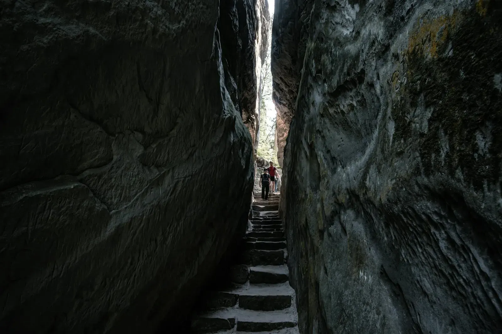 Hikers explore narrow rock passage in Český Raj, Czech Republic.