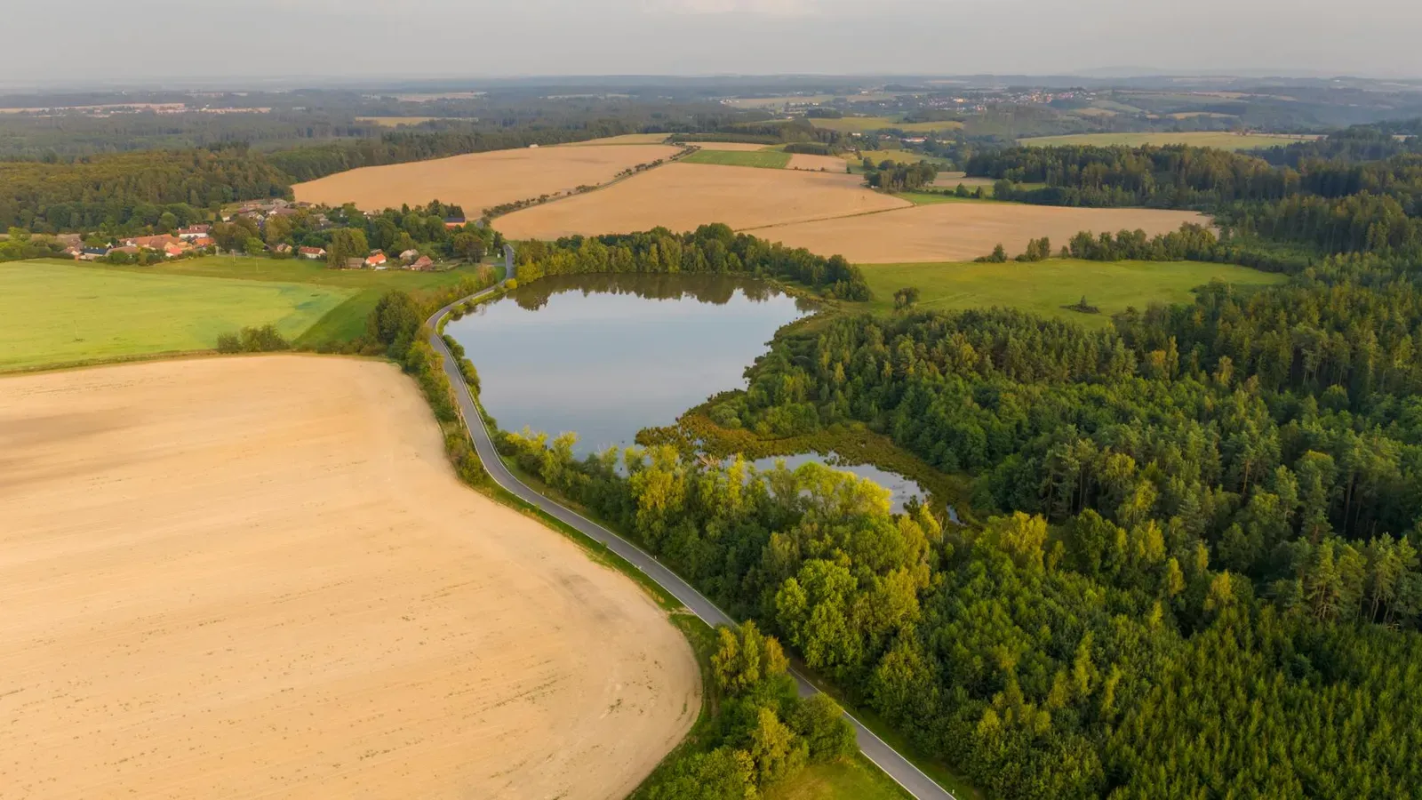 Aerial view of Chlístovice countryside with fields, forest, and lake.