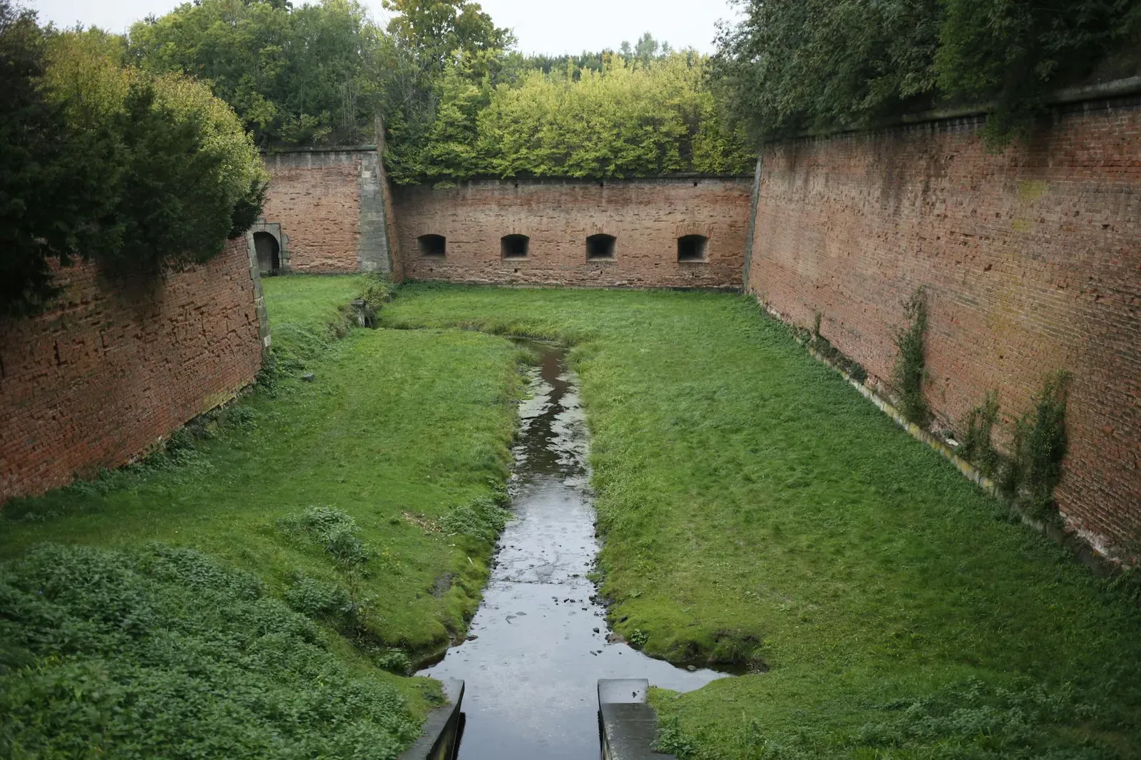 Serene view of historic Terezín fortress moat with lush greenery and brick walls.